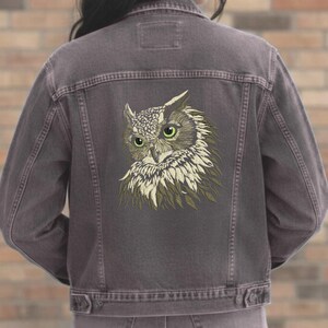 May include: A dark gray denim jacket featuring an embroidered owl design on the back. The owl has green eyes and a detailed feather pattern in shades of beige and olive green. The jacket has a classic button-up design.