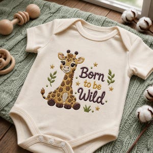 May include: A cream-colored short-sleeve baby bodysuit featuring an embroidered brown and tan giraffe. The text "Born to be Wild" is stitched in dark brown thread, accompanied by small gold stars and green leaf accents on the front chest.