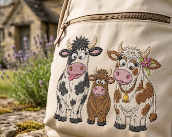 Puede incluir: Una mochila de lona beige con un diseño bordado de tres vacas de dibujos animados. La vaca de la izquierda es blanca y negra con la lengua fuera, en el centro un ternero marrón, y la de la derecha es marrón y blanca con una campana y una flor.