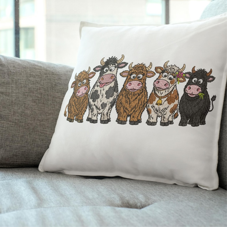 May include: A white square throw pillow featuring an embroidered illustration of five cartoon cows standing in a row. The cows vary in color, including brown, black and white spotted, and solid black, with one wearing a bell and another a flower.