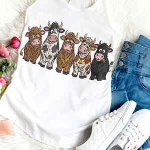 May include: A white tank top featuring a graphic print of five cartoon cows in a row. The cows include a brown shaggy cow, a black and white spotted cow with its tongue out, a light brown shaggy cow, a tan and white cow with a bell, and a black cow.