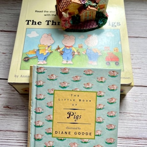 May include: Two children's books about pigs. The first book is titled "The Three Pigs" and features illustrations of three pigs. The second book is titled "The Little Book of Pigs" and features a blue cover with a pattern of pink pigs.