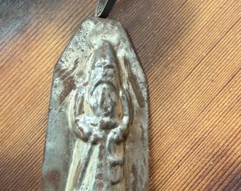 May include: A vintage metal mold featuring a raised relief of a bearded figure wearing a pointed hat and long robes. The mold has a weathered, oxidized silver-toned finish with visible rust patches and includes a dark fabric hanging loop at the top.
