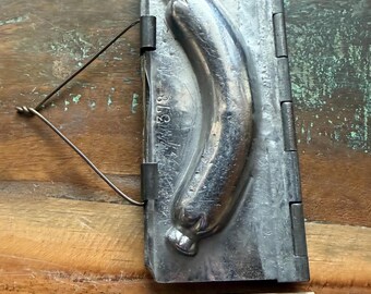 May include: A silver-colored metal sausage mold with a hinged design and a wire closure. The mold features a recessed sausage shape and the number 378 stamped on the surface. A wooden ruler is positioned below, showing a length of 4 inches.