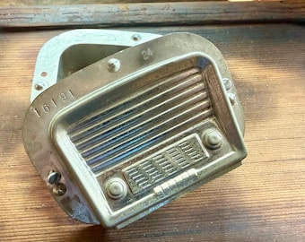 May include: A metallic, rectangular automotive dashboard radio speaker grille with a silver finish. The piece features horizontal slats, two circular knobs, a rectangular button array, and the stamped numbers 16191 and 24 on the frame.