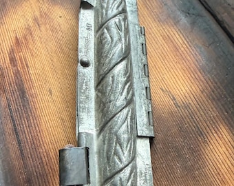 May include: A long, narrow, metallic baguette baking mold with a textured, diagonal-patterned surface. The silver-toned tool features a hinged side, two metal loops for securing, and the stamped text 04 and Stöckli on the side of the frame.