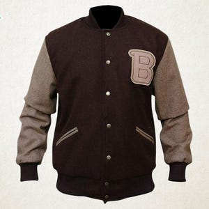 May include: A brown varsity jacket with gray sleeves. The jacket features a large letter "B" patch on the chest, two front pockets, and a button-up closure. The cuffs and collar are dark brown.