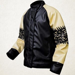 May include: Black and cream-colored leather jacket with a stand-up collar. The jacket features black sleeves with cream-colored shoulder panels and decorative black leaf-like cutouts. The jacket has a front zipper and a small pocket.