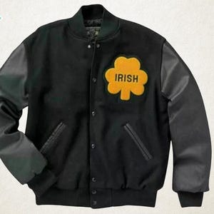 May include: Black varsity jacket with black leather sleeves and a yellow shamrock patch that reads "IRISH". The jacket has a button-up front and two front pockets. The "Luxury Jackets" logo is in the top left corner.