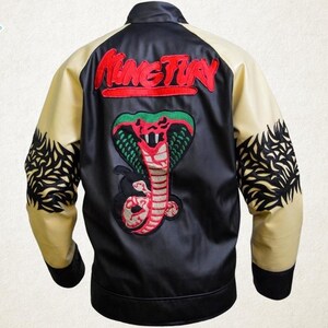 May include: Black and cream-colored jacket with a large cobra emblem and the word "King Fury" embroidered on the back. The jacket features black cuffs and a black bottom hem. The sleeves have a cream color with black decorative patterns.