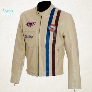 Op de afbeelding: Crème leren jas met zwarte kraag en ritssluiting. Voorzien van blauwe en bordeauxrode racestrepen en patches met de woorden "HEUER", "Firestone" en "Gulf". Een stijlvolle jas.