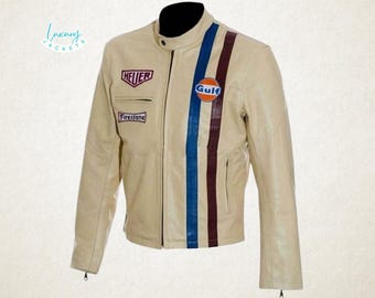 May include: Cream-colored leather jacket with a black collar and zipper closure. Features blue and maroon racing stripes, and patches with the words "HEUER", "Firestone", and "Gulf". A stylish jacket for a vintage look.