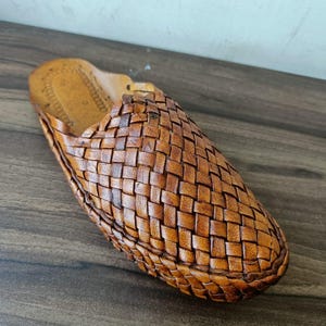 May include: A single brown leather slipper with a woven design. The slipper is made of a light brown leather and has a textured appearance. The slipper is designed for indoor use.