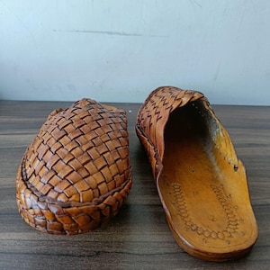 May include: Two brown leather woven sandals. One sandal is closed-toe, and the other is open-toe. The sandals are made of a light brown leather and have a woven design on the top. The soles are a darker brown.