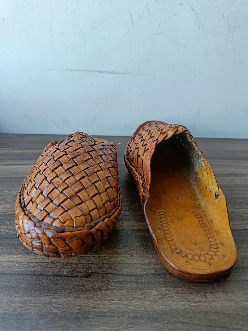 May include: Two brown leather woven sandals. One sandal is closed-toe, and the other is open-toe. The sandals are made of a light brown leather and have a woven design on the top. The soles are a darker brown.