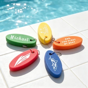 Pode incluir: Cinco porta-chaves de espuma de formato oval nas cores verde, amarelo, laranja, vermelho e azul. O verde diz Michael, o amarelo James, o laranja DAD, YOU FLOAT MY BOAT, o vermelho apresenta um gráfico de barco com JOHN e o azul tem um tubarão.