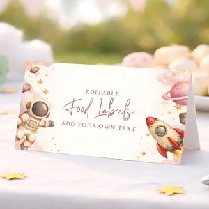 May include: A folded card with an outer space theme. The card features an astronaut, a rocket, planets, and stars. The text on the card reads "Editable Food Labels, Add Your Own Text."