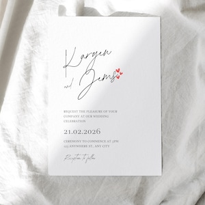 May include: A white wedding invitation with black script. The names "Vargen and Jems" are written in cursive, with small red hearts. The invitation includes the date, time, and location of the ceremony.
