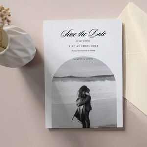 May include: A white wedding invitation card with the text "Save the Date" in a stylish script. The date "21st August, 2025" is displayed. A black and white photo of a couple embracing on a beach is featured.