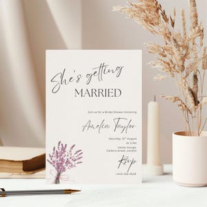 May include: A cream-colored bridal shower invitation with the text "She's getting MARRIED" in script. The invitation includes the name "Amelia Taylor", event details, and a lavender floral illustration. The design is elegant and minimalist.