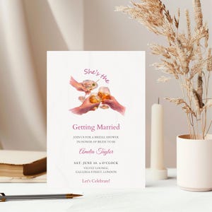 May include: A white invitation card with purple text, announcing a bridal shower. The card features a watercolor illustration of hands toasting with cocktails. The invitation includes the bride's name, date, time, and the location in London.