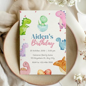 May include: A rectangular invitation card with a light beige background, featuring watercolor illustrations of colorful dinosaurs. The text "Aiden's Birthday" is displayed in blue and pink. Additional text includes the date, time, address, and RSVP information.