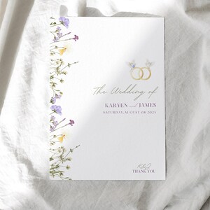 May include: A white wedding program with floral accents and gold rings. The text reads "The Wedding of KARYEN and JAMES SATURDAY, AUGUST 08 2025" and "THANK YOU". The program is decorated with purple and yellow flowers.
