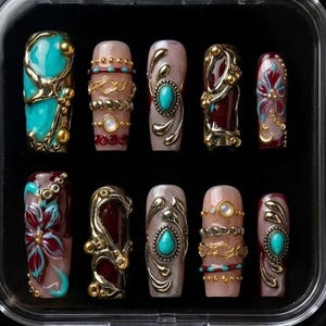 May include: A set of ten artificial nails in a clear plastic case. The nails feature various designs, including turquoise, gold, and burgundy accents. Some nails have floral patterns, while others have ornate metalwork and jewel embellishments.