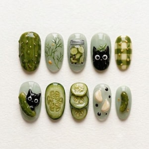 May include: A set of ten press-on nails featuring pickle-themed designs. The art includes a whole pickle, dill sprigs, a jar of sliced pickles, a black cat, green gingham, a cat with a pickle, cucumber slices, garlic cloves, and a small pickle.