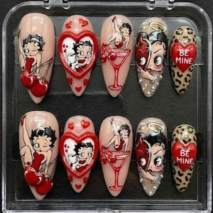 May include: A set of ten artificial nails with various designs. The designs include Betty Boop illustrations, heart shapes, and leopard print patterns. Some nails feature the text "BE MINE". The color palette includes red, black, and nude tones.