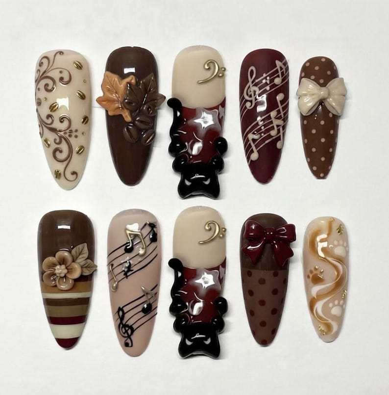 May include: A set of ten almond-shaped press-on nails featuring brown, cream, and burgundy color palettes. Designs include 3D coffee beans, leaves, bows, musical notes, a black cat silhouette, stripes, polka dots, floral accents, and paw prints.