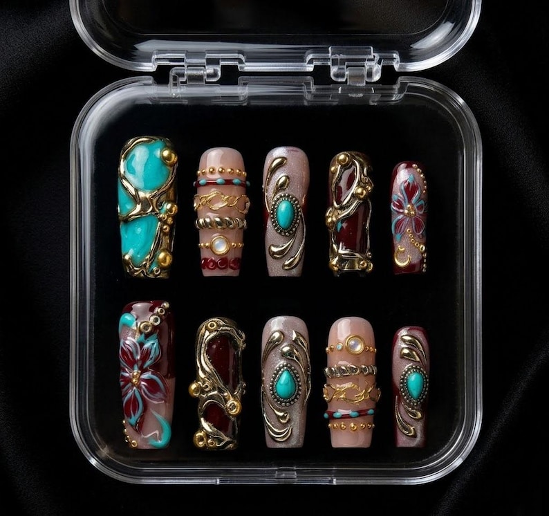 May include: A set of ten artificial nails in a clear plastic case. The nails feature various designs, including turquoise, gold, and burgundy accents. Some nails have floral patterns, while others have ornate metalwork and jewel embellishments.