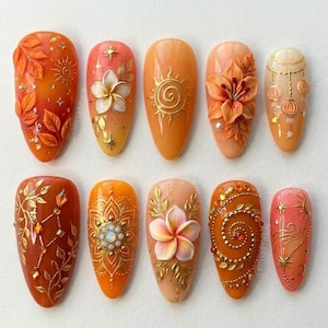 May include: A collection of ten almond-shaped artificial nails with intricate designs. The nails feature a variety of orange, peach, and gold tones, with detailed floral, sun, and geometric patterns. Some nails have 3D embellishments.