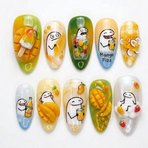 May include: A set of ten almond-shaped, decorated artificial nails. Each nail features a different design with a mango theme, including mango slices, a mango popsicle, and cartoon characters. The color palette includes yellow, green, and orange.