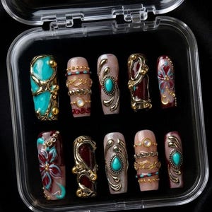 May include: A set of ten artificial nails in a clear plastic case. The nails feature various designs, including turquoise stones, gold embellishments, and floral patterns. The nails are in shades of teal, burgundy, and nude.
