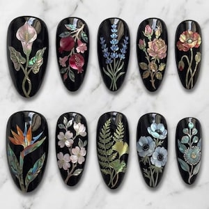 May include: A collection of ten black, oval-shaped nail art designs. Each nail features a different floral or botanical design, including calla lilies, pomegranates, lavender, roses, and poppies, with iridescent accents.