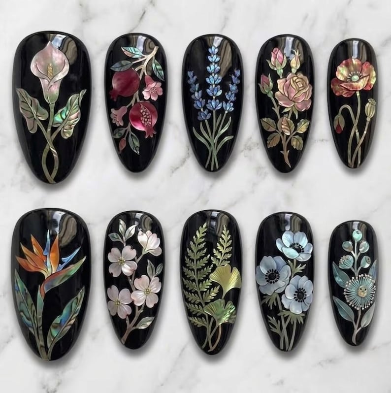 May include: A collection of ten black, oval-shaped nail art designs. Each nail features a different floral or botanical design, including calla lilies, pomegranates, lavender, roses, and poppies, with iridescent accents.
