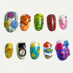May include: A set of ten colorful, decorated artificial nails. Designs include a watermelon, a star, a house, red stripes, pink stars, yellow and orange shapes, a black cat with a clock, blue stars, fish, and a purple bear.