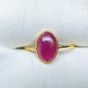 Può includere: Un anello d'oro con una gemma ovale rosa intenso. La gemma è incastonata in una lunetta d'oro e il gambo dell'anello è un semplice e sottile design in oro. L'anello è esposto su un tessuto bianco strutturato.