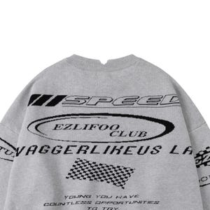 May include: A gray sweater with black text and graphics. The word "SPEED" is above an oval that says "EZLIFOO CLUB". Below is "VAGGERLIKEUS LA" and a checkered flag graphic. The bottom text reads "YOUNG YOU HAVE COUNTLESS OPPORTUNITIES TO TRY."