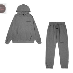 May include: A gray hoodie and matching sweatpants set. The hoodie has a front pocket and a hood. The sweatpants have a drawstring waist. Both pieces have the word "ESSENTIALS" printed on them.