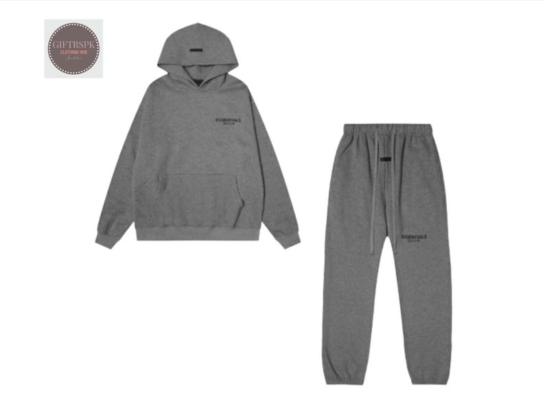 May include: A gray hoodie and matching sweatpants set. The hoodie has a front pocket and a hood. The sweatpants have a drawstring waist. Both pieces have the word "ESSENTIALS" printed on them.