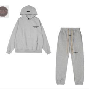 May include: A light gray hoodie and matching sweatpants set. The hoodie has a hood and the word "ESSENTIALS" printed on the chest. The sweatpants have a drawstring and the same logo. A casual, comfortable outfit.