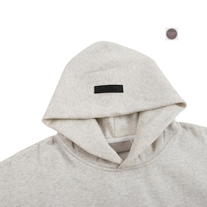 May include: A light gray hoodie with a drawstring neckline and a hood. A small black rectangular label is sewn on the hood. The hoodie is made of a soft, textured material.