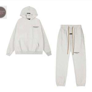May include: A light grey hoodie and matching sweatpants set. The hoodie has a hood and a front pocket. The sweatpants have a drawstring waist. Both pieces have the word "ESSENTIALS" printed on them in black.