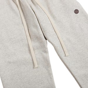 K&ouml;nnte beinhalten: Hellgraue Jogginghose mit Kordelzug in der Taille und einem kleinen runden Aufn&auml;her am Bein. Die Hose hat eine lockere Passform und ist aus einem weichen, bequemen Material gefertigt. Der Kordelzug ist cremefarben.