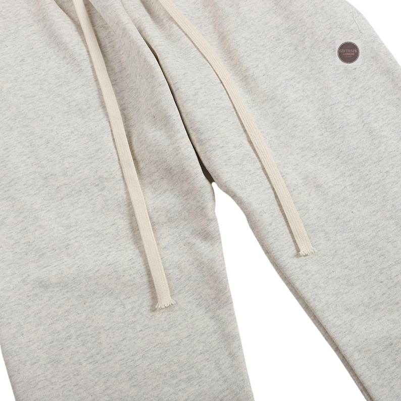 K&ouml;nnte beinhalten: Hellgraue Jogginghose mit Kordelzug in der Taille und einem kleinen runden Aufn&auml;her am Bein. Die Hose hat eine lockere Passform und ist aus einem weichen, bequemen Material gefertigt. Der Kordelzug ist cremefarben.