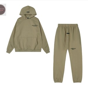 May include: A matching olive green hoodie and sweatpants set. The hoodie has a hood, a front pocket, and the word "ESSENTIALS" printed on the chest. The sweatpants have a drawstring waist and the word "ESSENTIALS" printed on the leg.