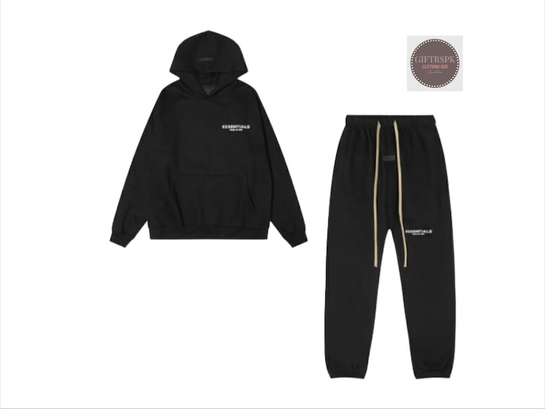 May include: Black hoodie and sweatpants set. The hoodie has a hood and a front pocket. The sweatpants have a drawstring waist. Both pieces have the word "ESSENTIALS" printed in white.