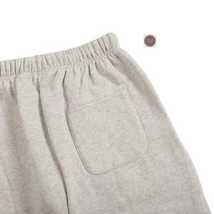 K&ouml;nnte beinhalten: Nahaufnahme von hellgrauen Sweatshorts mit elastischem Bund und einer einzelnen Ges&auml;&szlig;tasche. Die Shorts bestehen aus einem weichen, bequemen Material, ideal f&uuml;r Freizeitkleidung. Die Shorts haben eine neutrale Farbe.